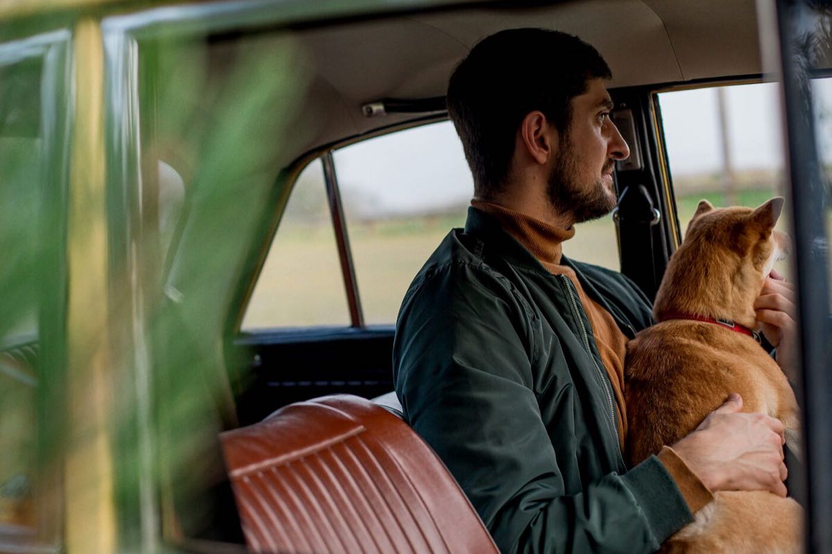 A man driving with a dog riding in the passenger seat beside him.