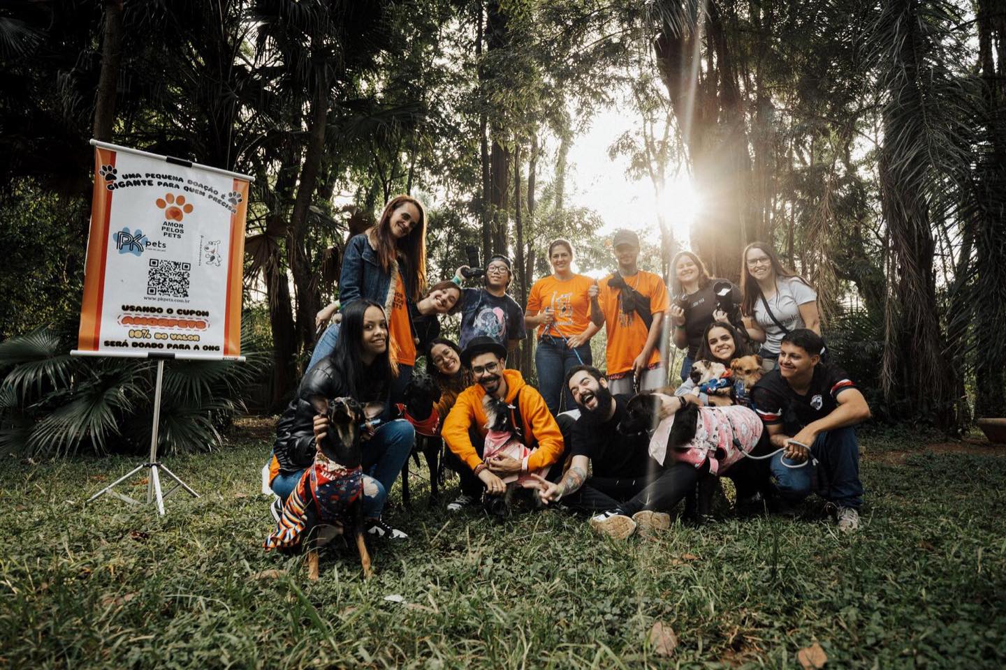 A large group of volunteers gathered outdoors with dogs available for adoption.